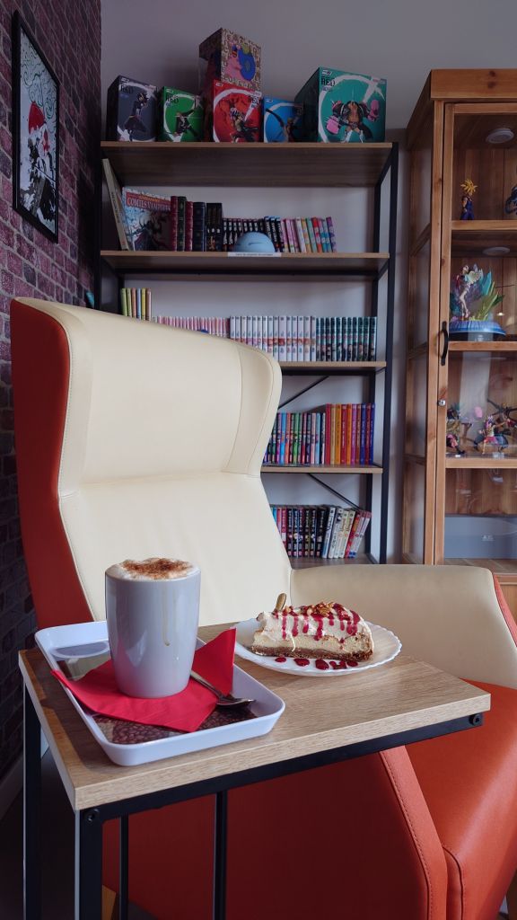 Une photo d’un sofa dans le café avec des manga sur une étagère en arrière plan